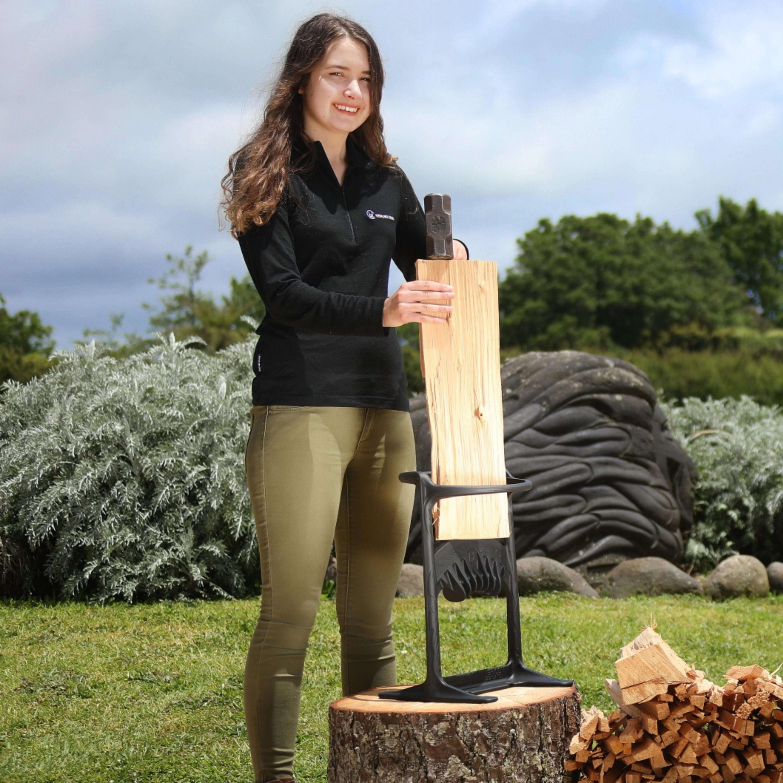 Ayla Hutchinson using her invention, the kindling cracker to split firewood on a chopping block